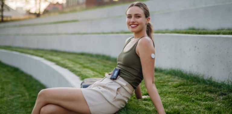 A woman sitting outside. She is wearing an insulin pump.