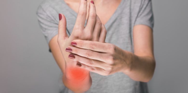 A woman holding her wrist, which has red coloring over it to represent joint pain.