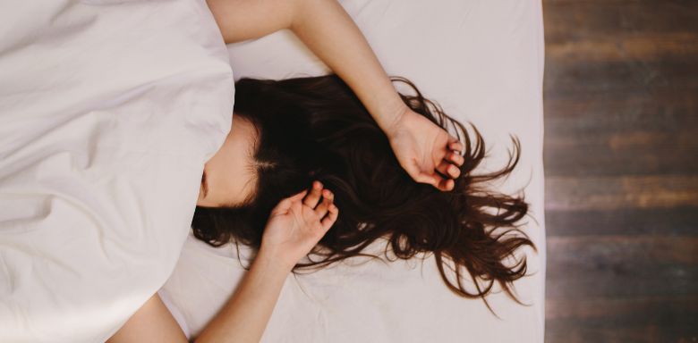 A woman laying down with her hands above her head, and a blanket covering her face.