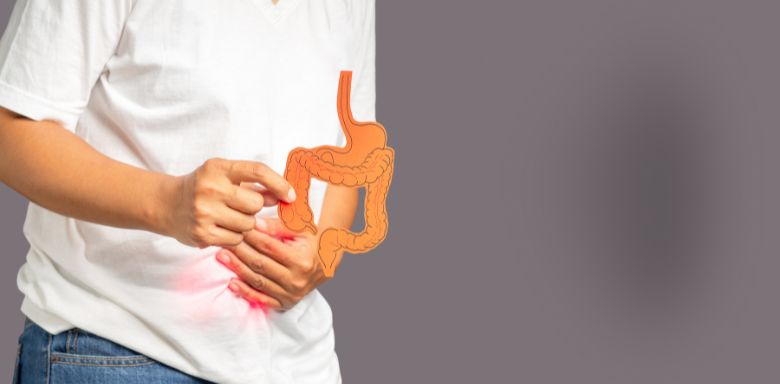 A man holding one hand to his stomach. In the other hand, he's holding a paper diagram of intestines.