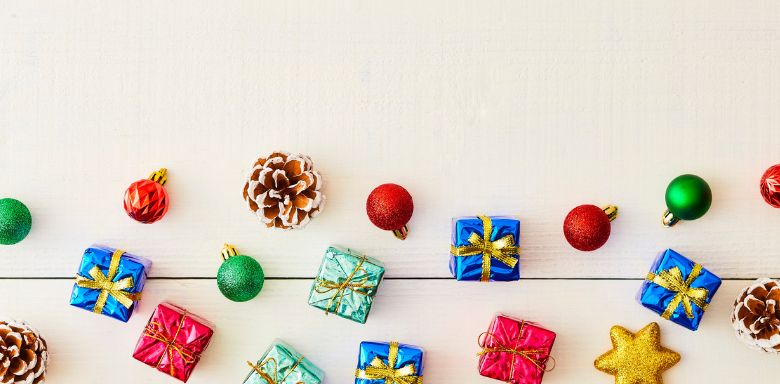 Tiny wrapped gifts n a white surface with Christmas tree ornaments.